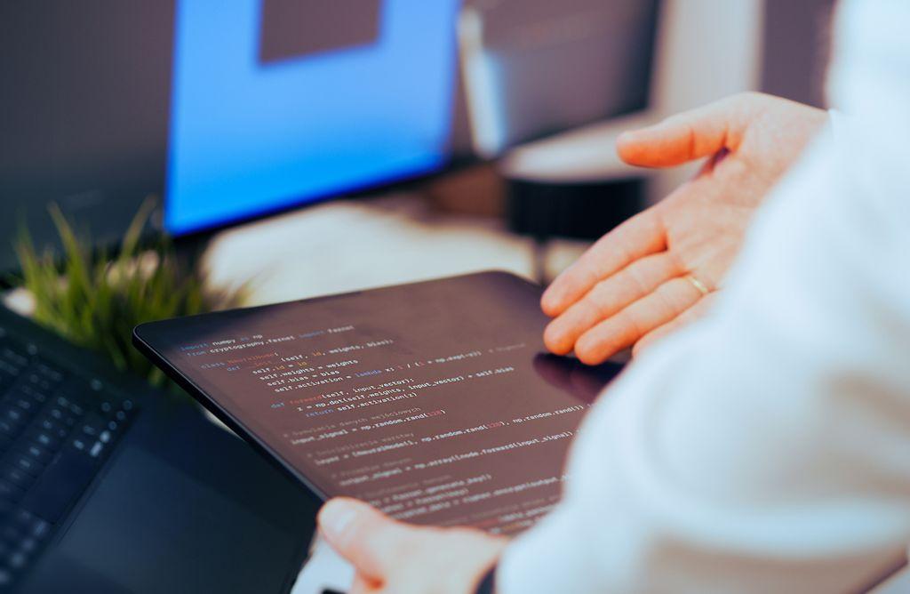 Desarrollador revisando código en una tableta junto a un computador